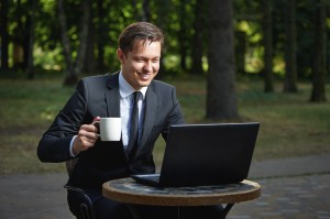 Handsome smiling businessman holding coffee cup in the park cafe