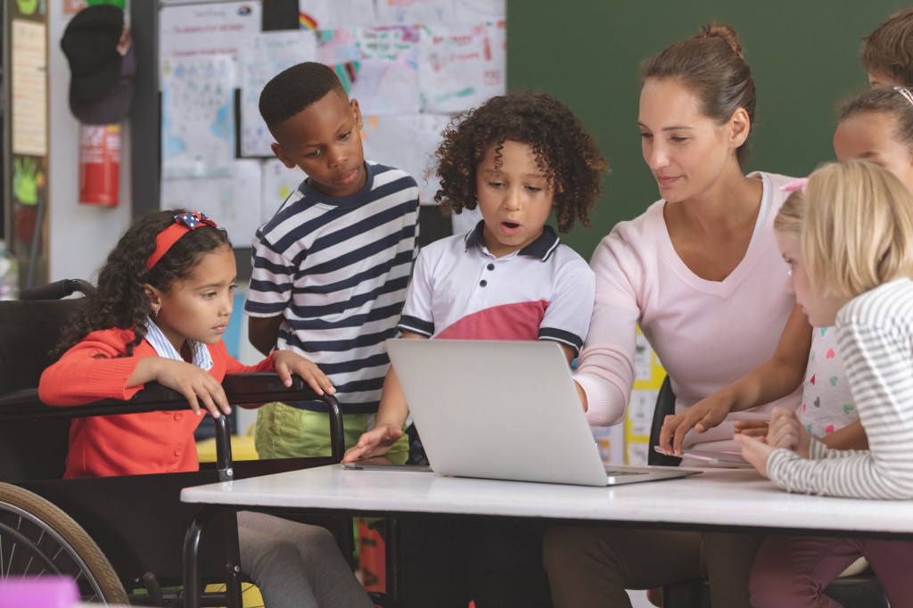 Teacher and school kids discussing over laptop in classroom