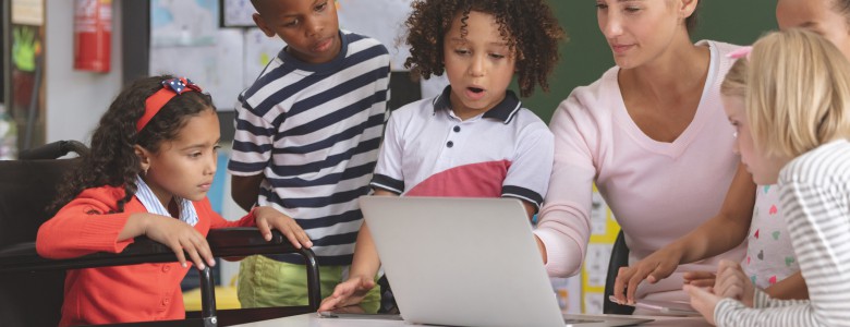 Teacher and school kids discussing over laptop in classroom