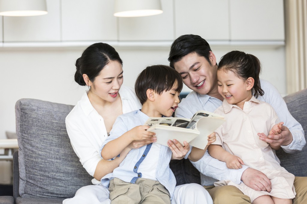 A pair of parents reading a children's storybook with their two sons and daughters - stock photo