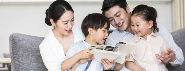 A pair of parents reading a children's storybook with their two sons and daughters - stock photo