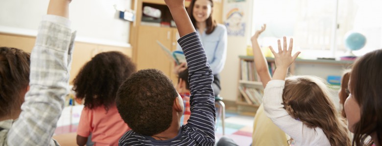 Elementary school kids raising hands to teacher, back view