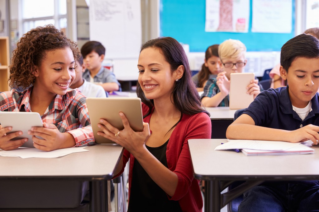 Teacher helping kids with computers in elementary school