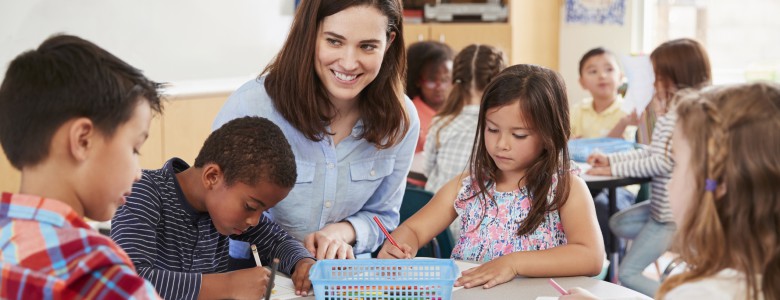 Teacher sitting at table with young school kids in classroom