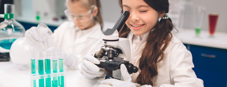 Two little kids in lab coat learning chemistry in school laboratory. Young scientists in protective glasses making experiment in lab or chemical cabinet. Looking through the microscope