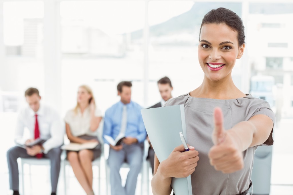 Businesswoman gesturing thumbs up against people waiting for interview