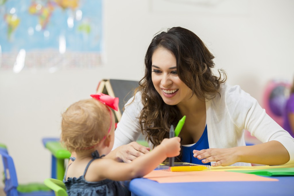 Pretty daycare teacher helps toddler with coloring project