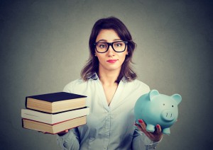 Young woman with stack pile of books and piggy bank full of debt rethinking future career path